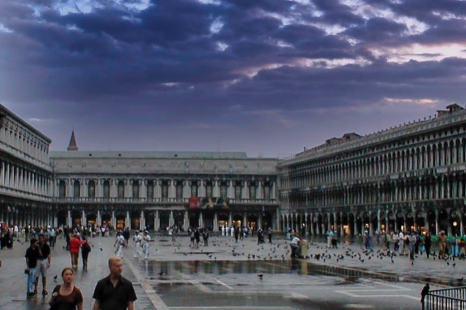 A view into St. Mark’s Square in Venice after the rain  with the dark storming sky reflected in the puddles and tourists roaming the square.