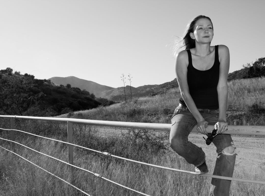 Black and white photo of a girl straddling a fence.