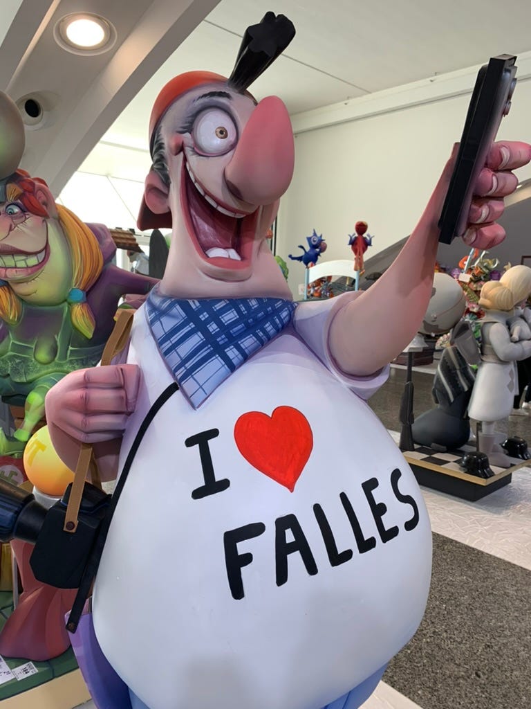 A cartoonish life-size figure of a man with a I heart Fallas, a cell phone and other tourist trappings