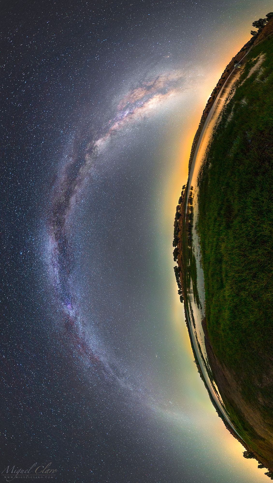 The Milky Way arches over a curved landscape of the Earth, alight with bright veins of stars. 