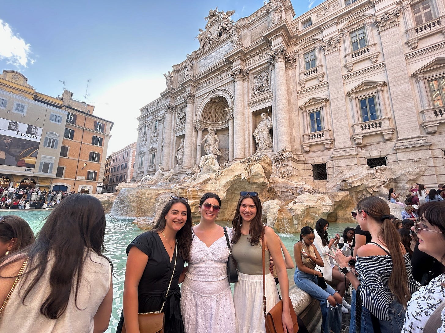 Three 20-something women posed in front of Rome's Trevi Fountain, surrounded by crowds