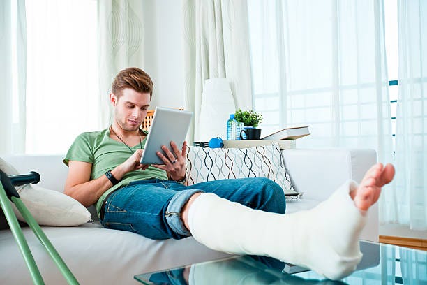 Young man with broken leg at home Young man with broken leg sitting on sofa at home and using digital tablet.  rehabilitation technologies stock pictures, royalty-free photos & images