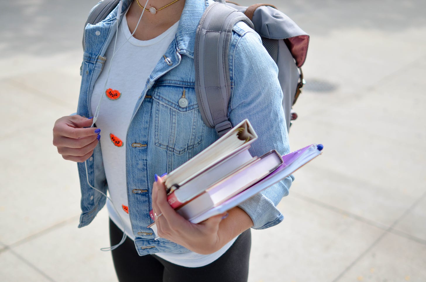 photo of the torso of a student wearing a jean jacket holding a stack of books