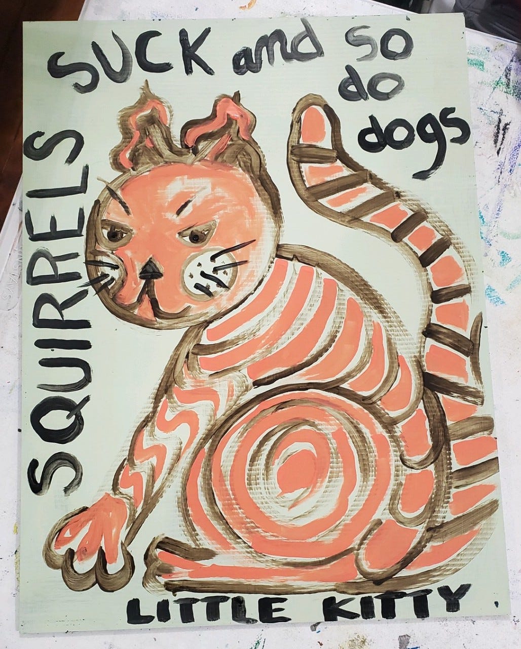 Painted sign of an orange striped cat that says "squirrels suck and so do dogs" with "little kitty" written at the bottom