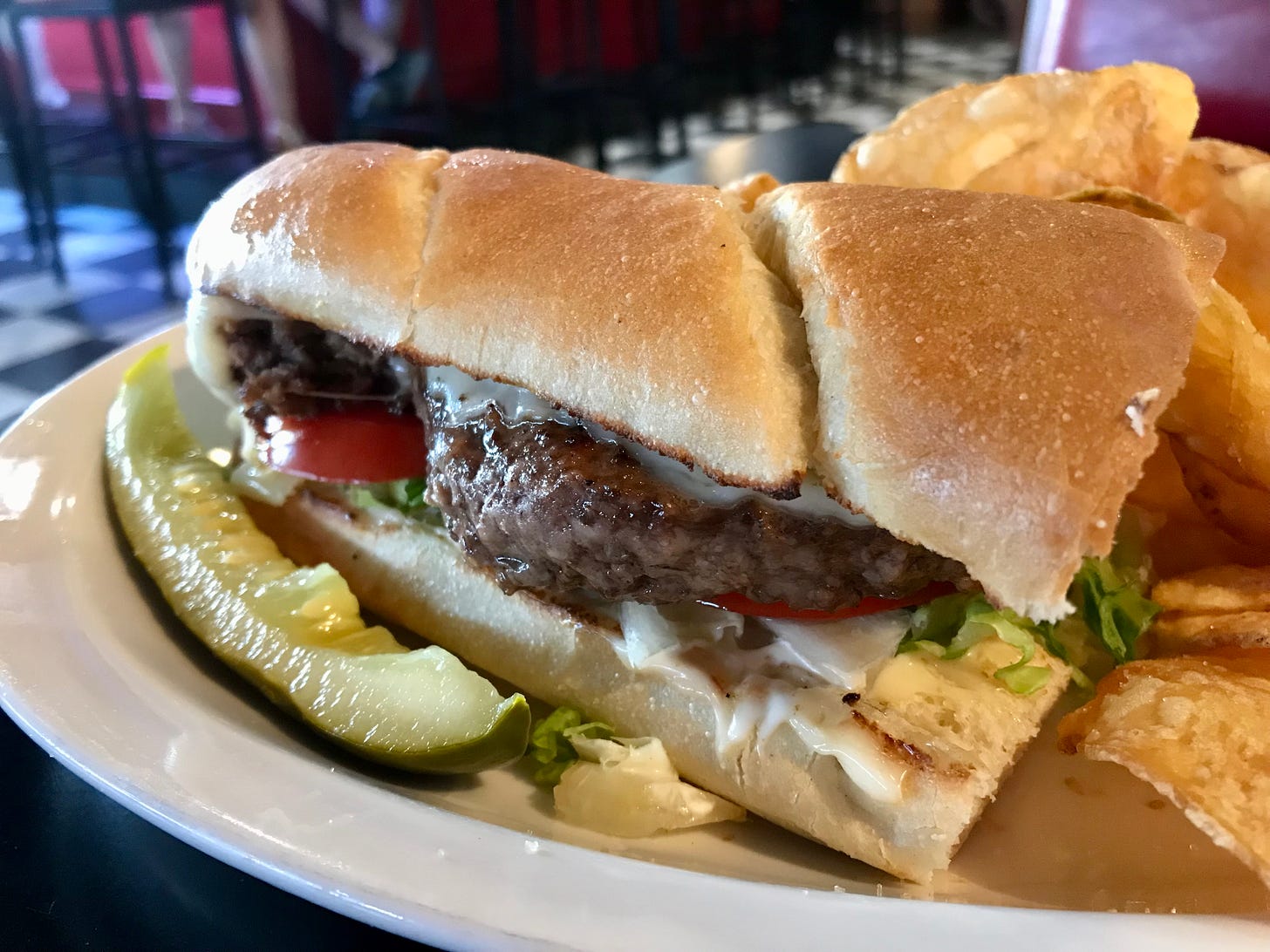 Half a cheeseburger sub with thick patty. Pickle and chips on side.