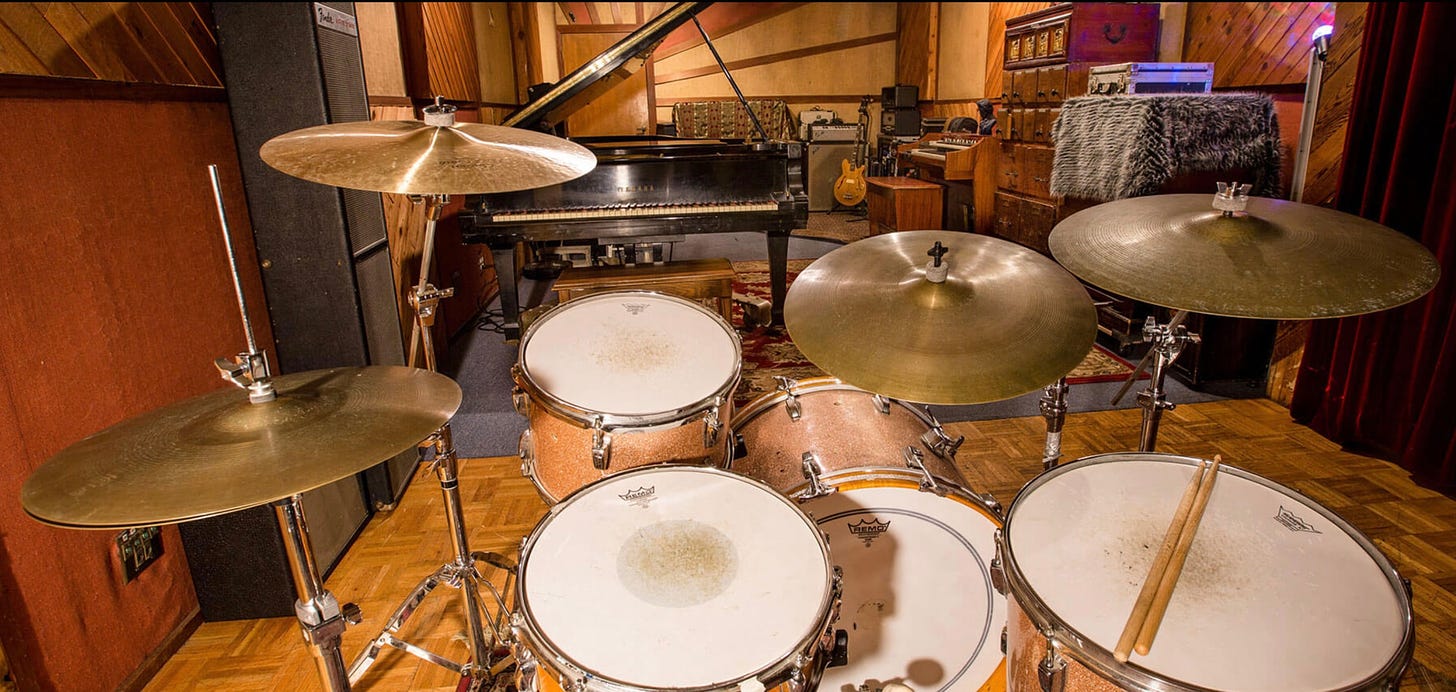 A recording studio with a drum kit, gibson guitar and grand piano