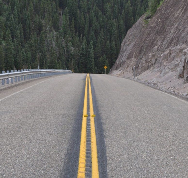 gray concrete road between green trees during daytime