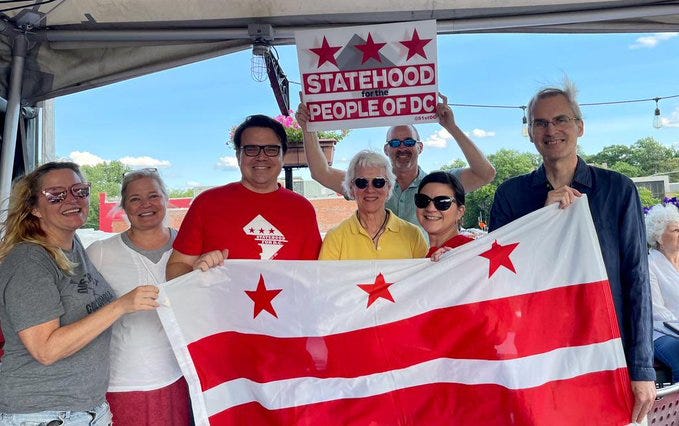 Photo of seven people on CP Bar and Grill Rooftop bolding a DC Flag and one person is holding a sign saying statehood for the people of DC.