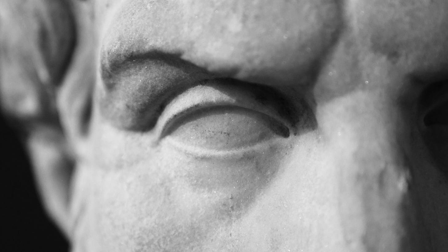 Black-and-white photo encompassing a single eye of a sculpture of the head of the ancient Greek philosopher Epicurus.