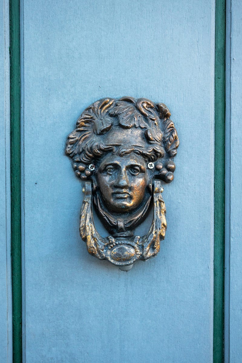 Door knocker with the image of a person, made out of metal.