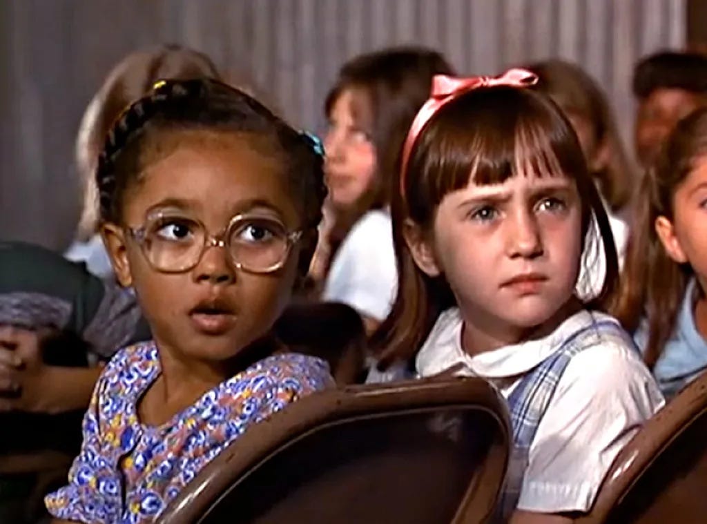 "Matilda" main character and her friend Lavender with shocked and confused faces in an auditorium scene from the 1996 film.