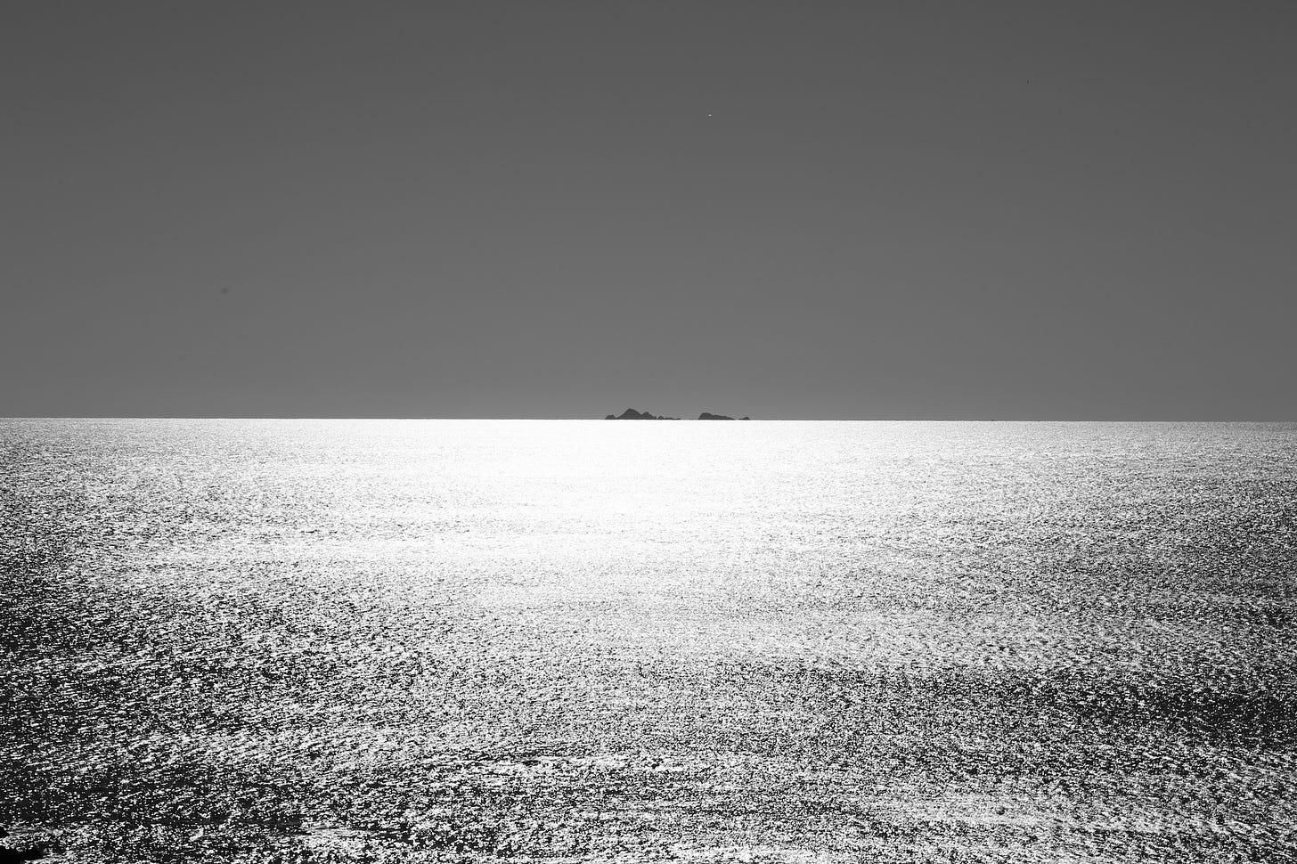 Photo of islands on a distant horizon seen across a sea reflecting the sun.
