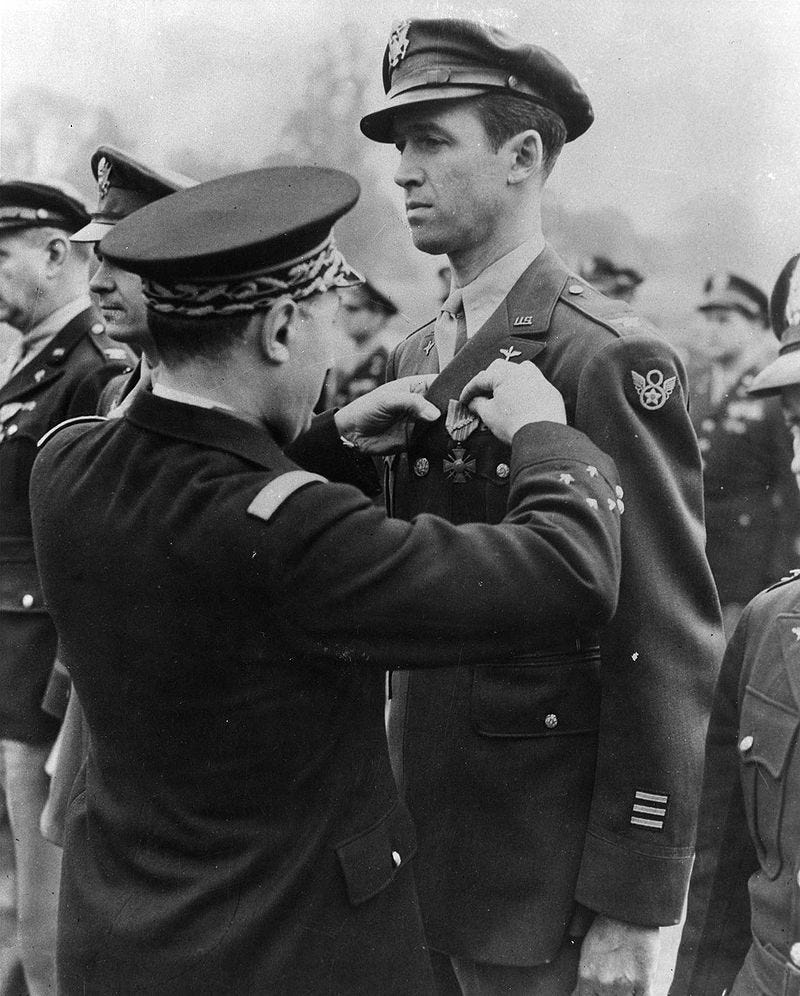 A military officer pinning an award to Stewart's decorated military jacket, among other uniformed soldiers