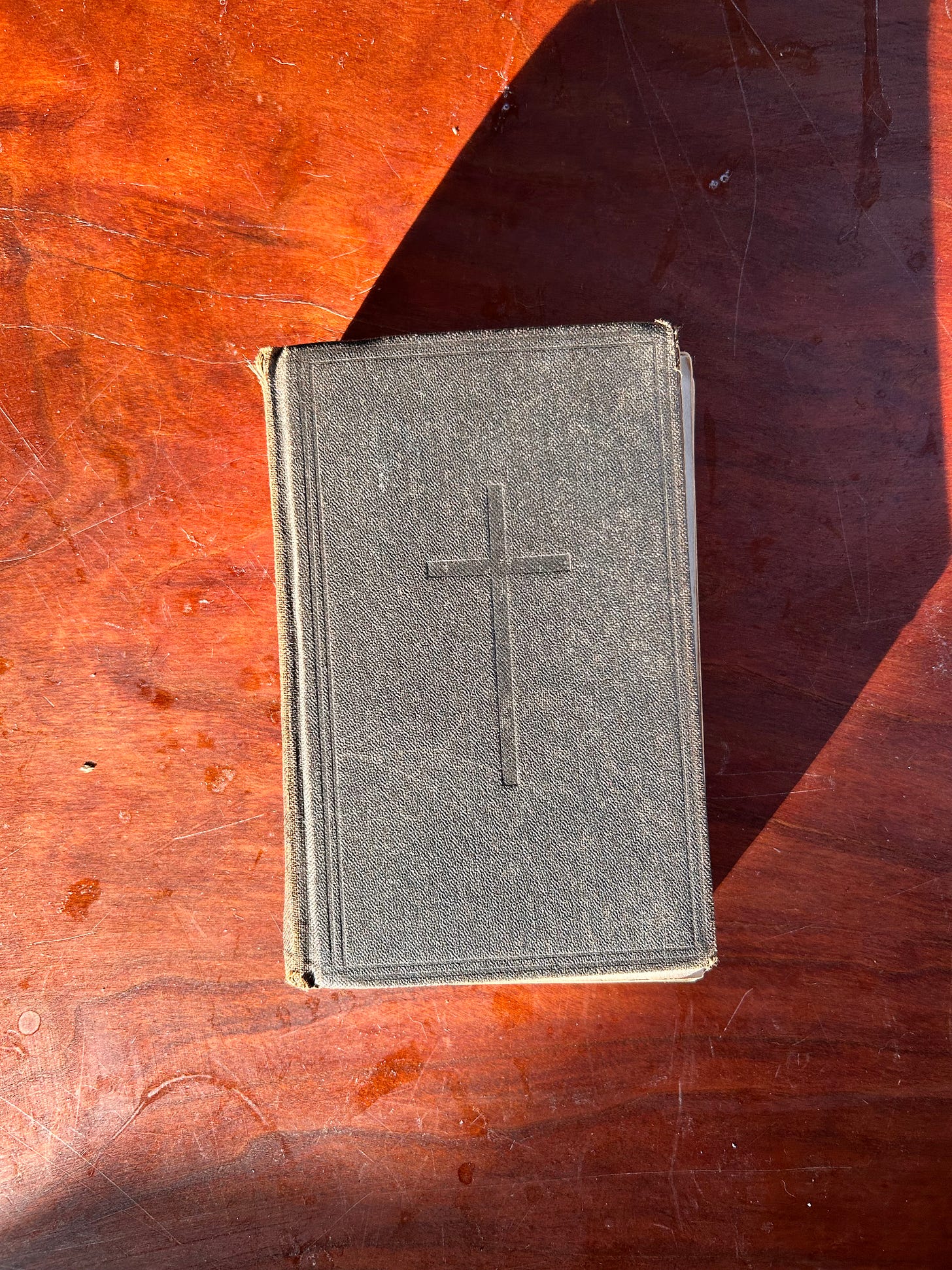 A prayer book, closed, featuring a cross on the front. Sitting on top of a wooden table.