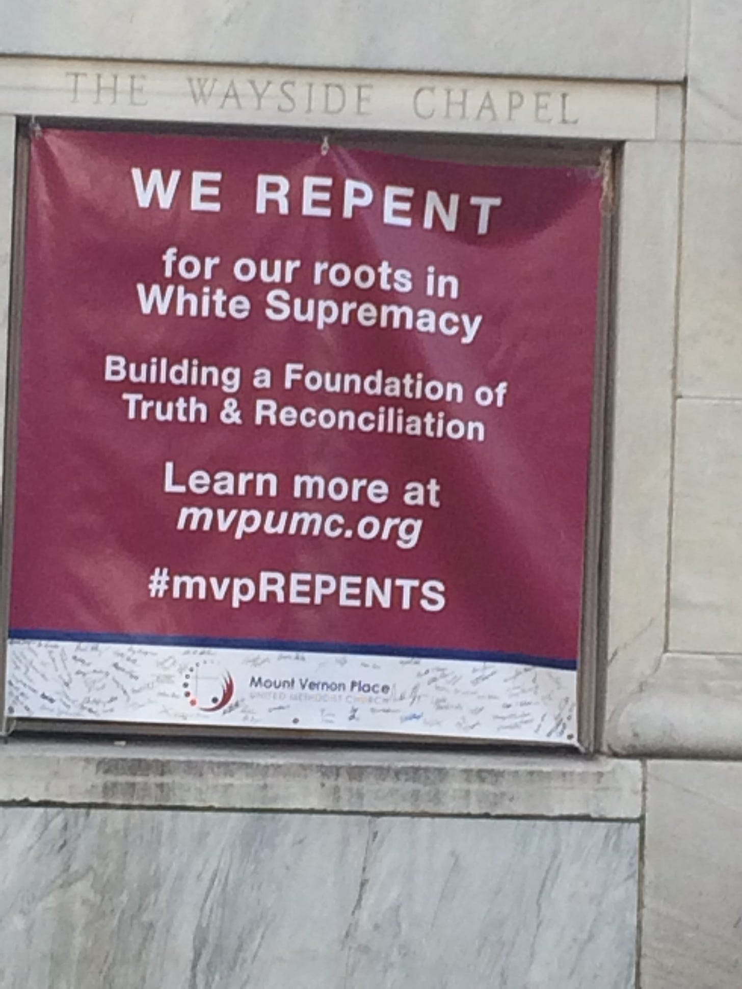 A sign mounted on the side of the Mount Vernon Place United Methodist Church says "WE REPENT for our roots in White Supremacy Building a Foundation of Truth & Reconciliation Learn more at mvpumc.org #mvpREPENTS