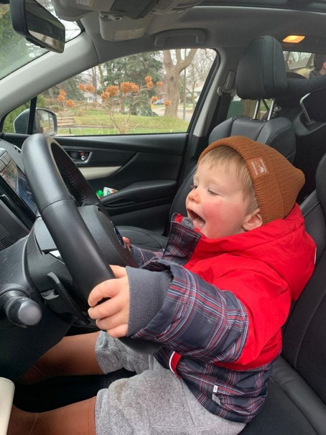 A toddler sits in the driver's seat of a car 