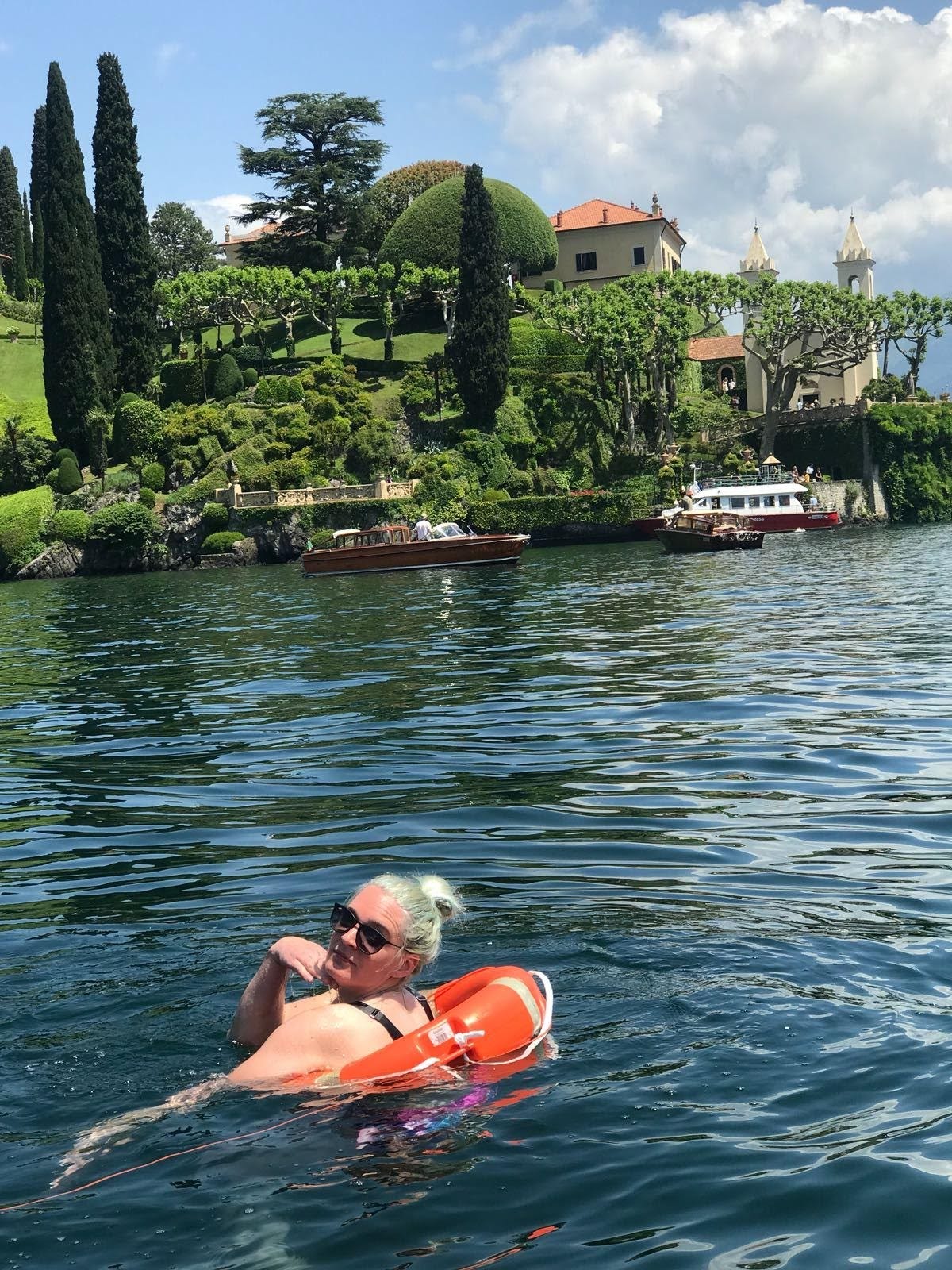 Wearing sunglasses and posing suggestively as I wear a safety ring around my waist in the water, the beautiful backdrop of Lake Como show rich green hills, private yachts and stunning Italian villa. 