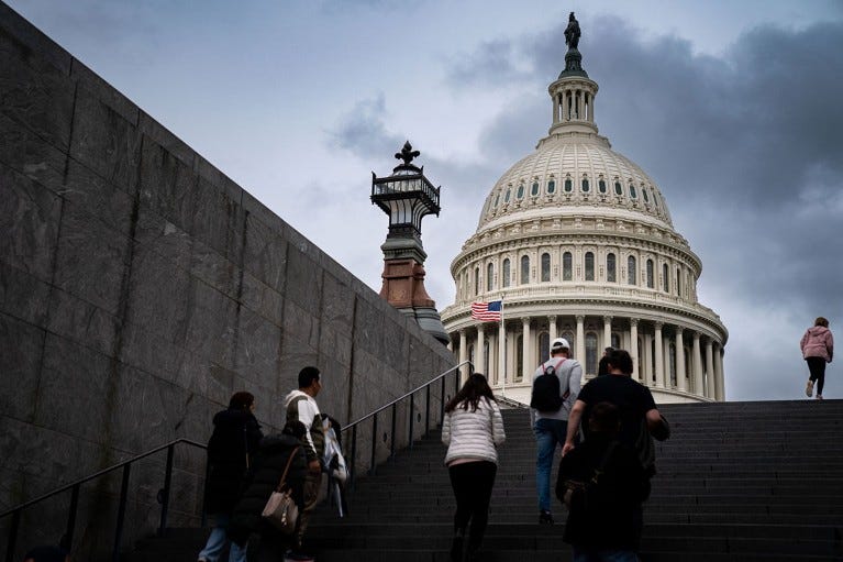 Visitors are cast in silhouette at the top of stairs near the US Capitol.