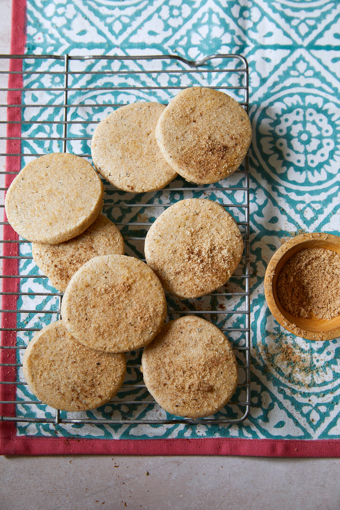 A rack of Black Pepper & Vanilla Chai Shortbread cookies, over a blue and red patterned cloth, with a bowl of chai-black pepper spice blend alongside.