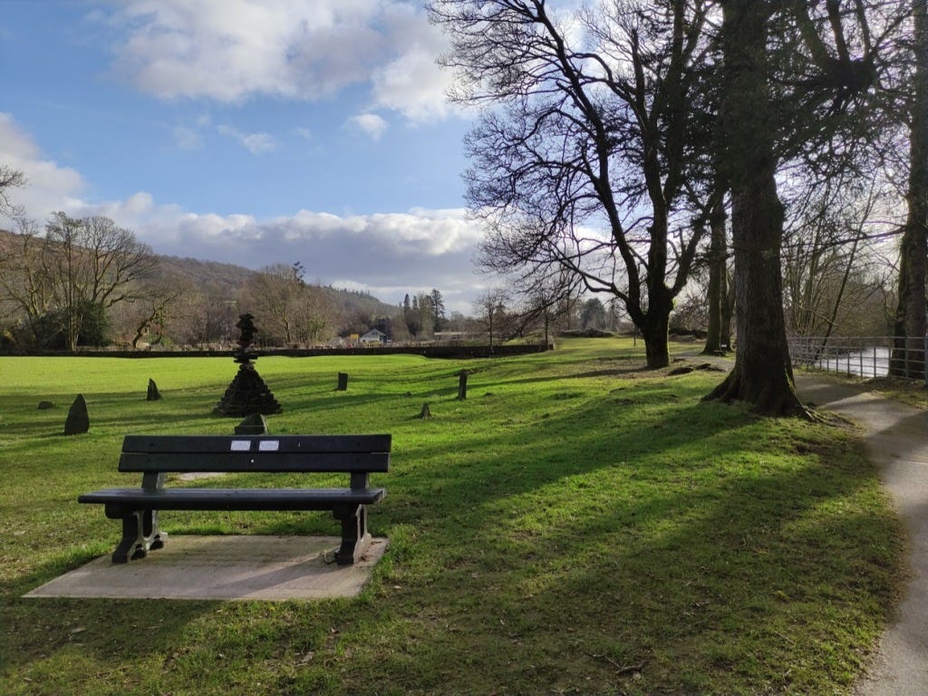 A bench in the foreground, with green grass and a tarmacked path to the right.