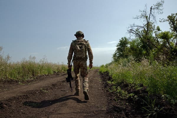 A soldier walks along a dirt path, his back to the camera.