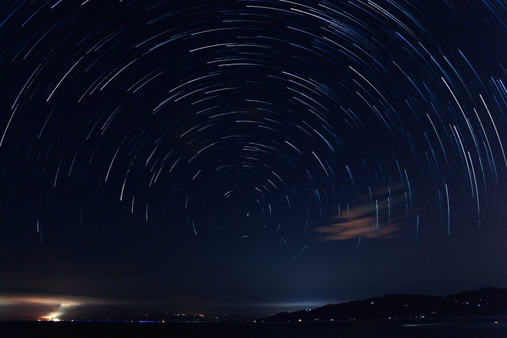 Night sky with star trails making a circle around Polaris, near the horizon
