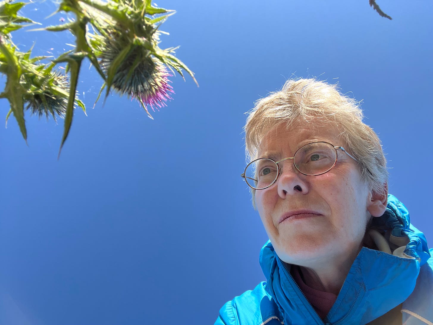 Portrait of photographer Michela Griffith seen with a spear thistle (Cirsium vulgare) against an azure sky