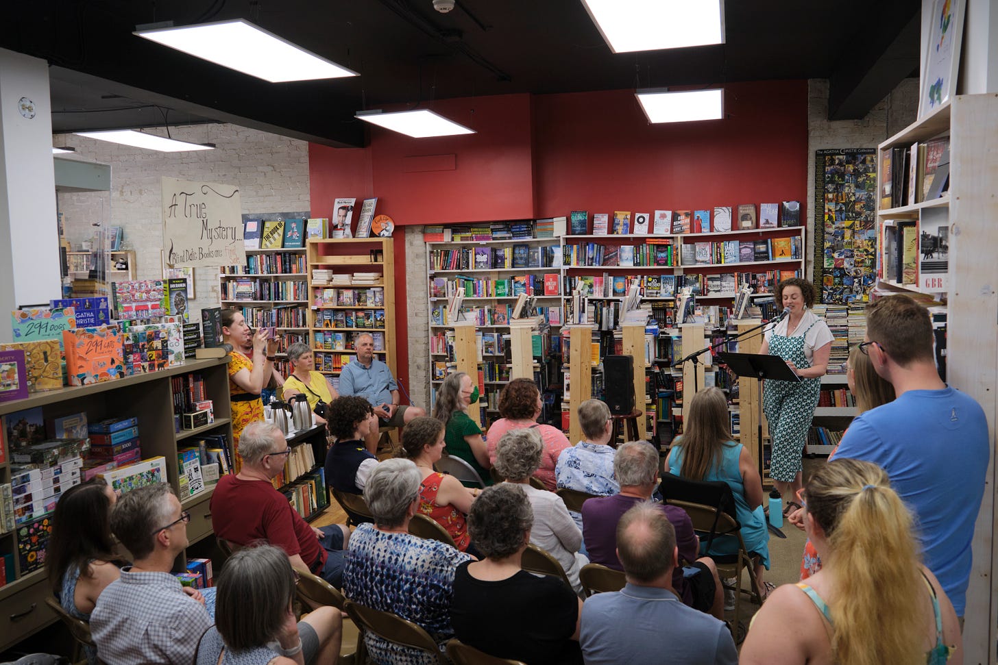 A bunch of people gathered in a bookstore in the cozy space between lots of book and shelves, an author reading her book at the front!