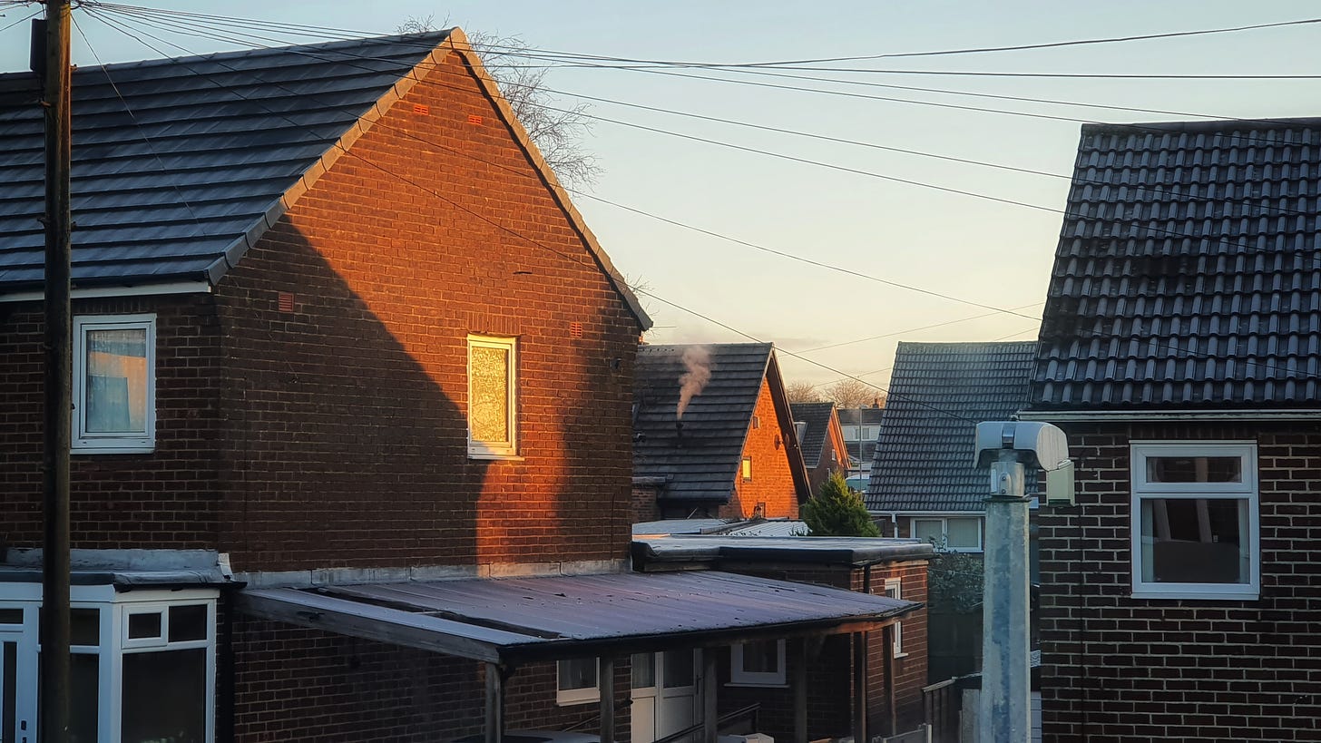 photo of houses early one frosty morning. Smoke rising from chimneys and orange gable ends where early morning sun makes the bricks glow.