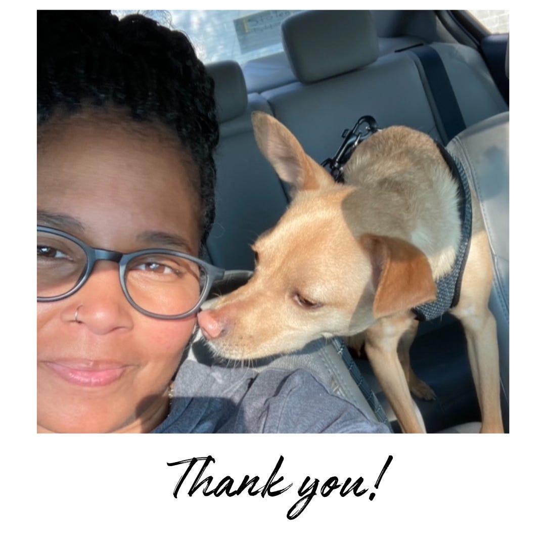 A picture of myself with my hair in a bun and grey glasses. My tan chihuahua is leaning in to lick my cheek as we sit in the car.