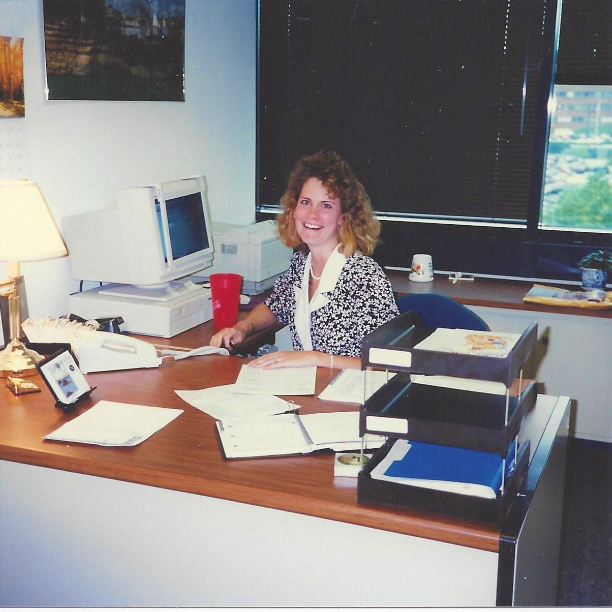 A 20-something woman sits behind a desk at work in a scene from the 1990s