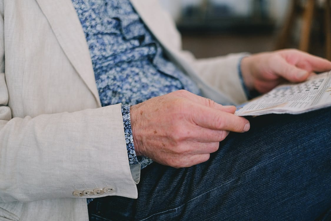 Free Close-up of a senior adult's hand holding a newspaper in a calm setting. Stock Photo