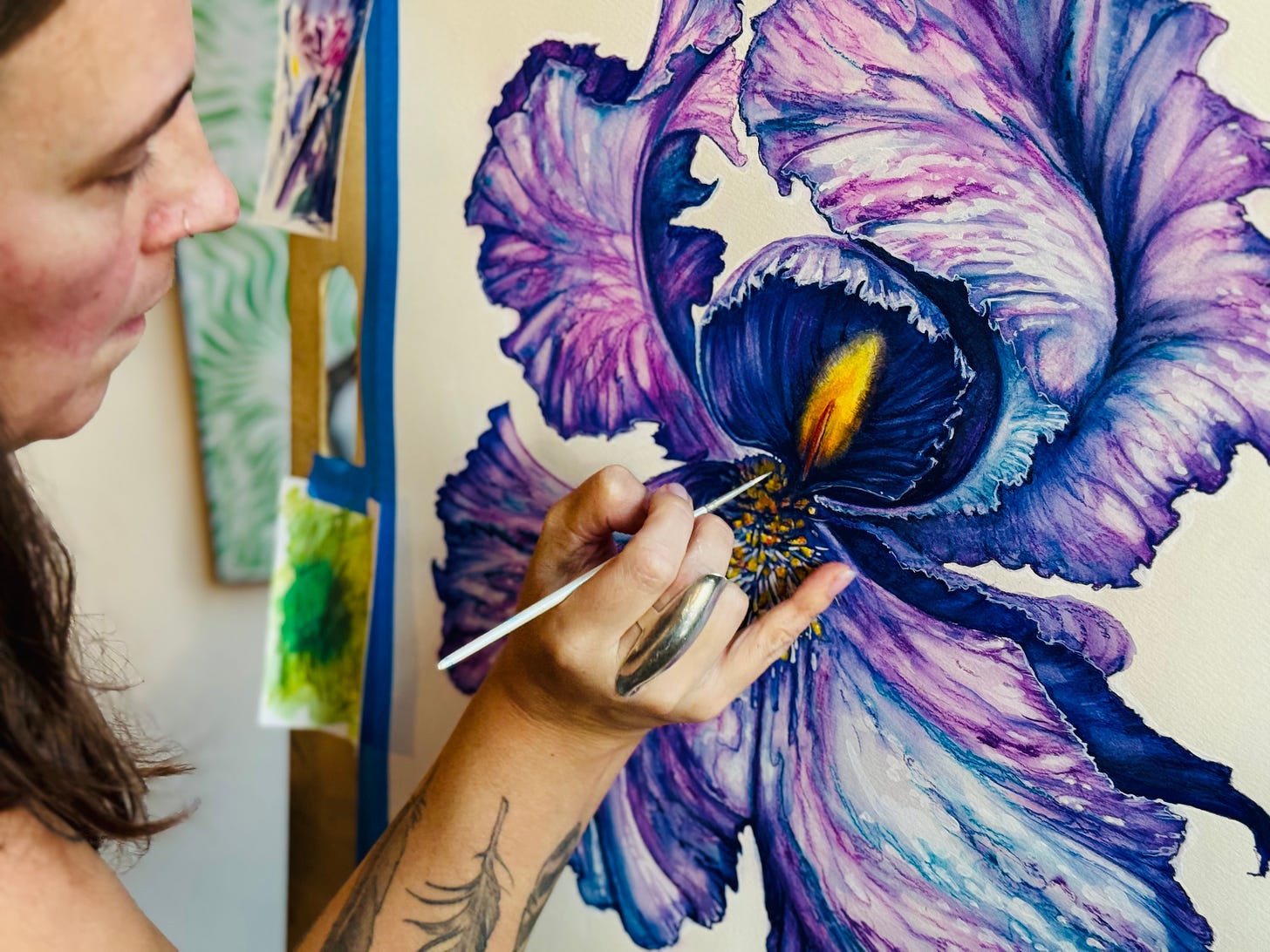 Lisette paints with a small paintbrush on a work in progress watercolor of a vibrant purple iris.