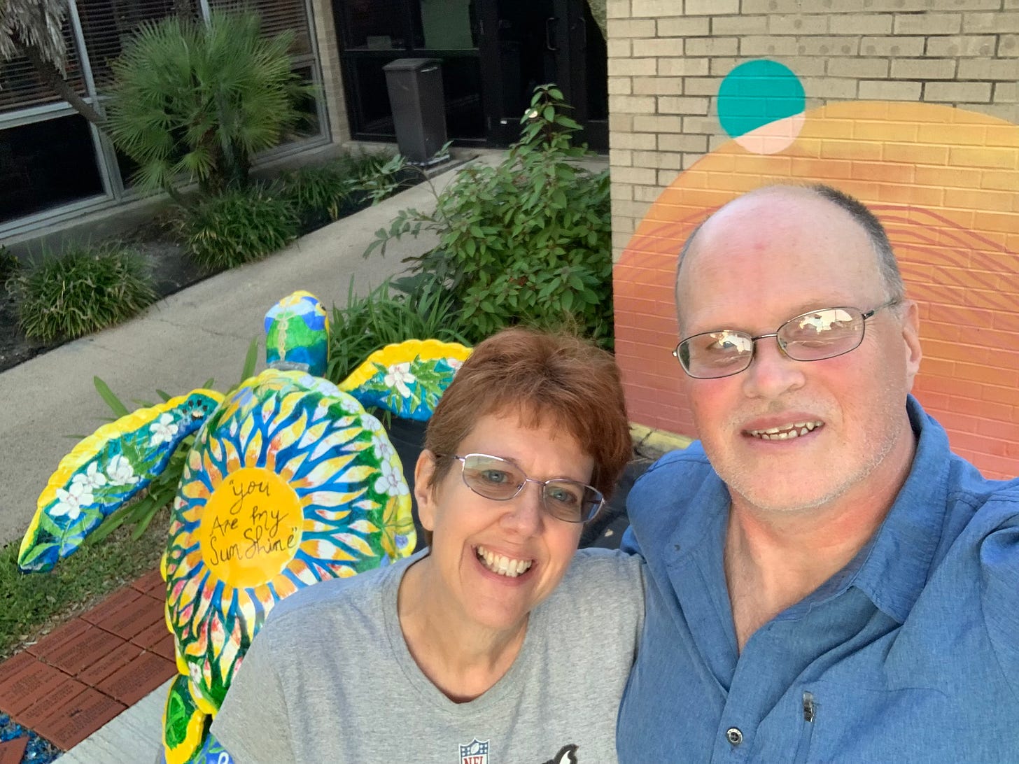Author Wendi Gordon with her husband Steve next to a colorful sea turtle sculpture with "You are my sunshine" painted on it