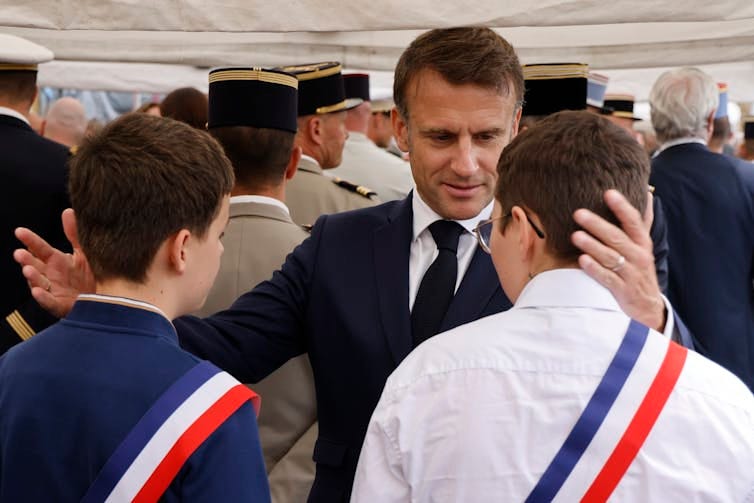 A dark-haired man embraces two young men, who are photographed from behind.