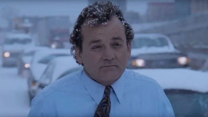 Bill Murray in Groundhog Day, standing outside without a jacket during a snow storm in front of a traffic jam.