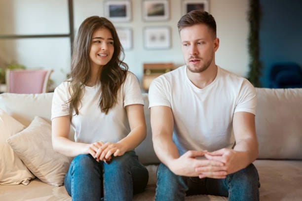 Young Couple Man And Woman Sitting On The Sofa Both Looking Embarrassed  Grimacing Mood Stock Photo - Download Image Now - iStock