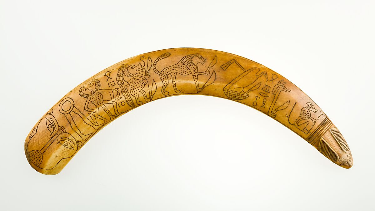 A curved ivory hippo tusk is carved with animal figures and the hieroglyphic phrases "protection of day" and "protection of night.”