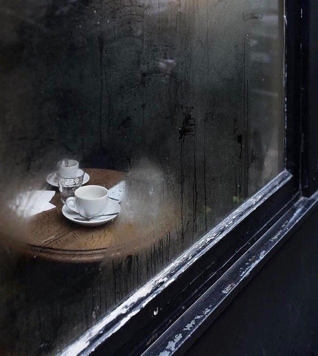 This may contain: a cup and saucer sitting on top of a wooden table next to a window