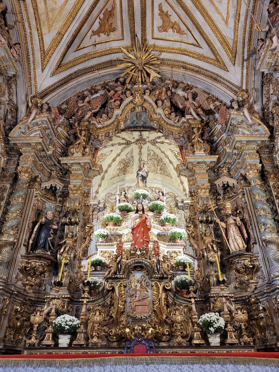 o altar riquíssimo em detalhes, com santos nas laterais, anjos na parte de cima, Jesus à frente e a Nossa Senhora bem no alto, tudo muito revestido de ouro.