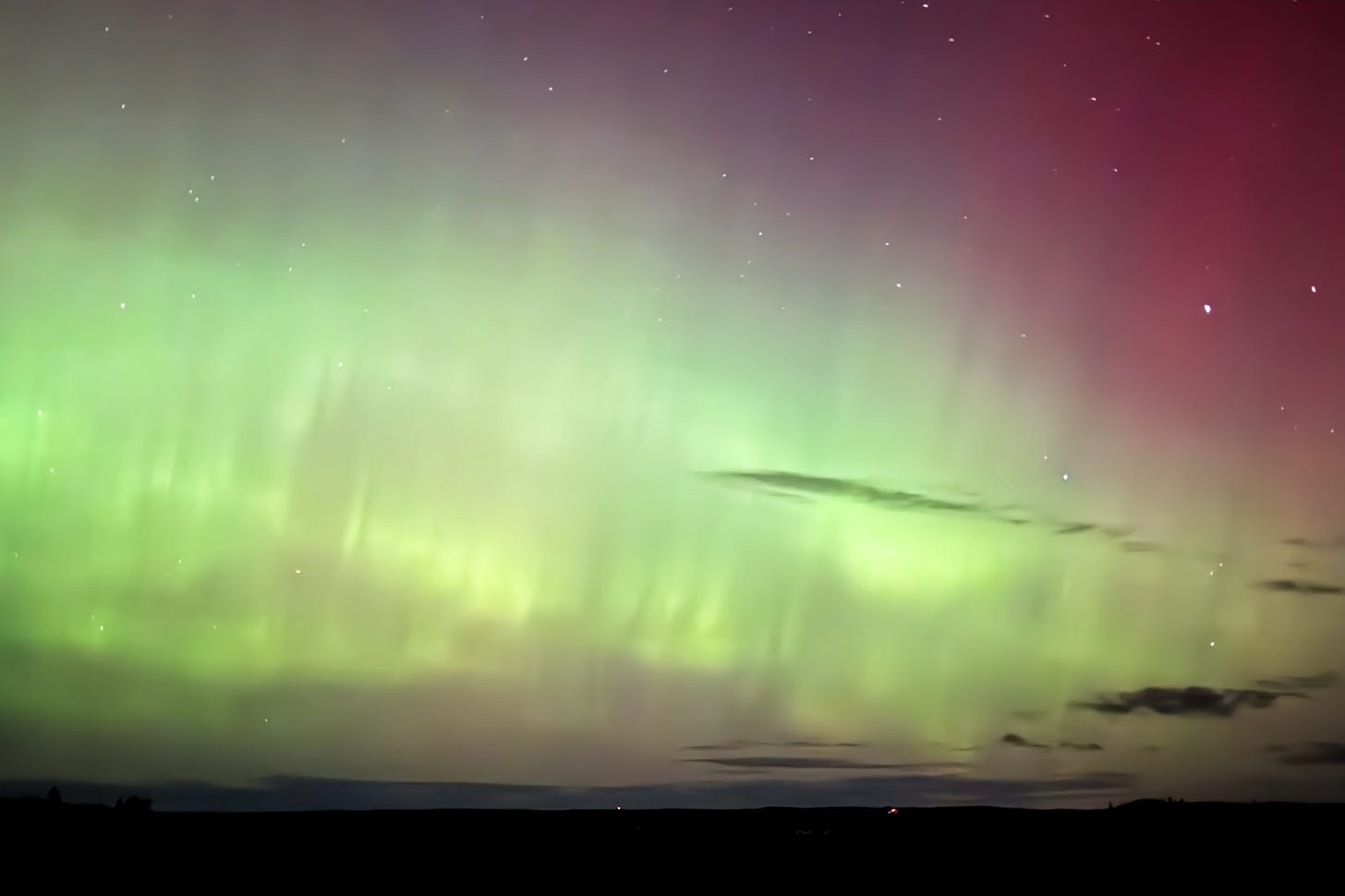 Green aurora bands wave into pink over the horizon.