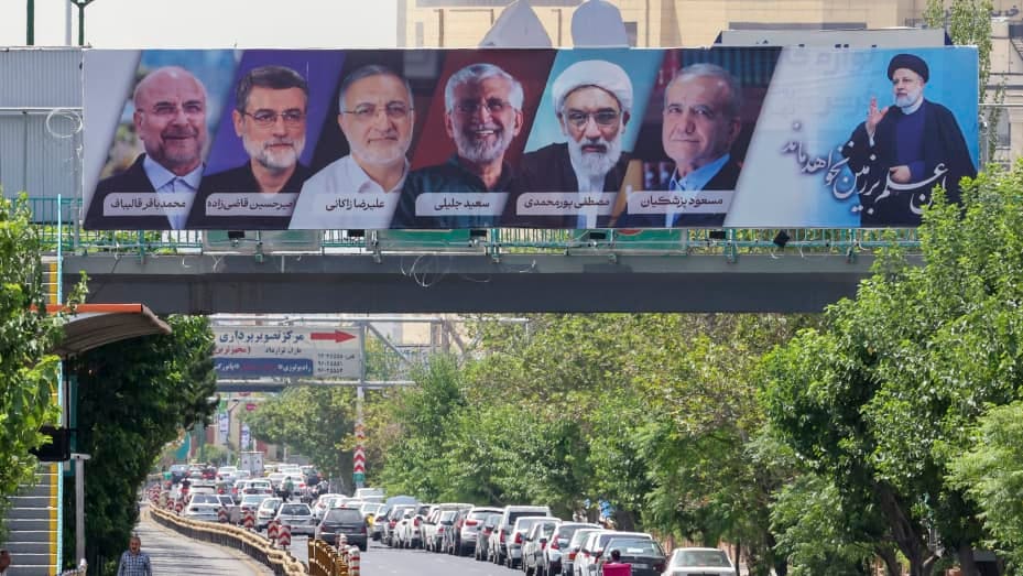 Vehicles move past a billboard displaying the faces of the six presidential candidates (L-R) Mohammad Bagher Ghalibaf, Amirhossein Ghazizadeh-Hashemi Alireza Zakani, Saeed Jalili, Mostafa Pourmohammadi and Masoud Pezeshkianin in the Iranian capital Tehran on June 29, 2024. Iran's sole reformist candidate Masoud Pezeshkian and ultraconservative Saeed Jalili are set to go to runoffs after securing the highest number of votes in Iran's presidential election, the interior ministry said. (Photo by ATTA KENARE / 