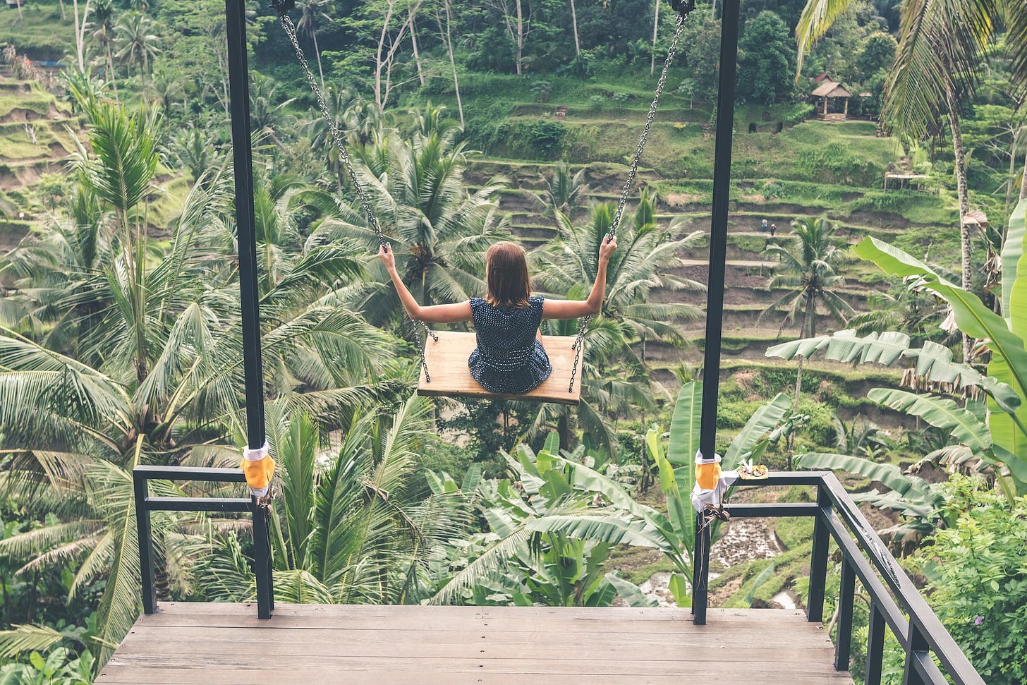 Girl on a swing high up over tropical plantation