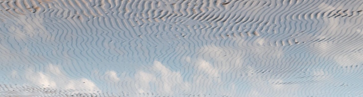 A photograph of a blue sky, reflected in a pool of water in the desert.