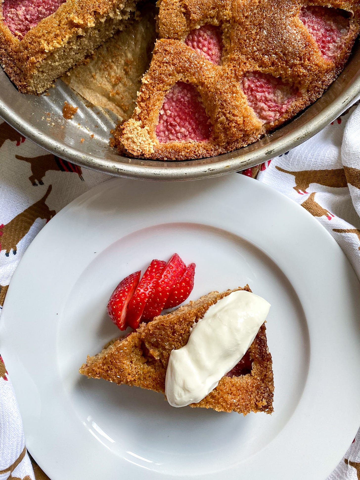 Strawberry spelt cake with a piece cut out on plate with sliced strawberries and cream