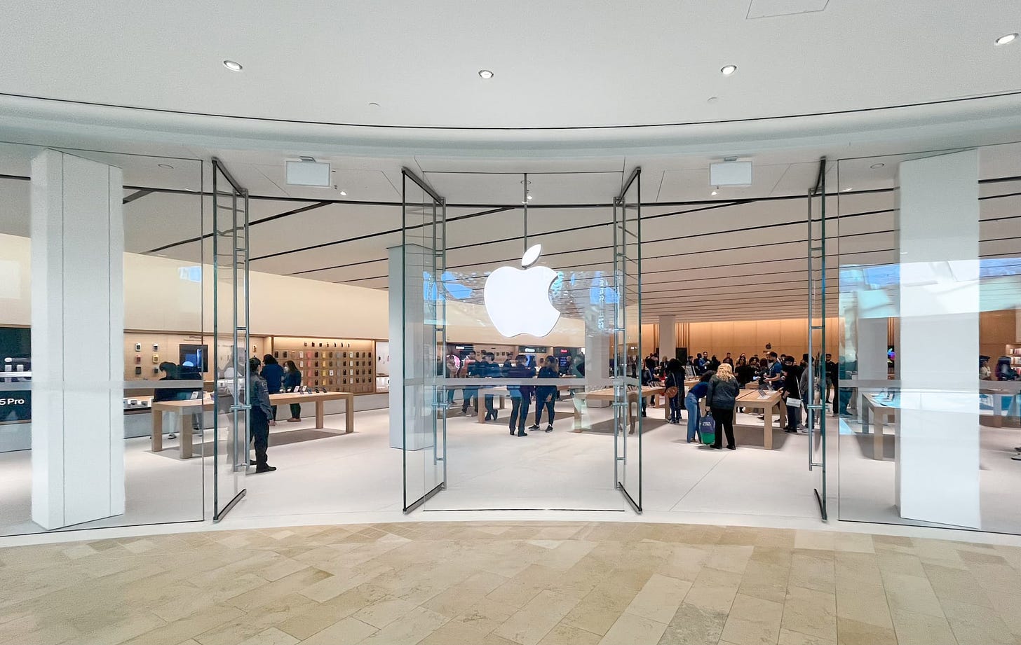 The exterior of Apple Square One, viewed from the mall corridor. A large, glowing Apple logo hangs in the center, framed by two sets of doors.