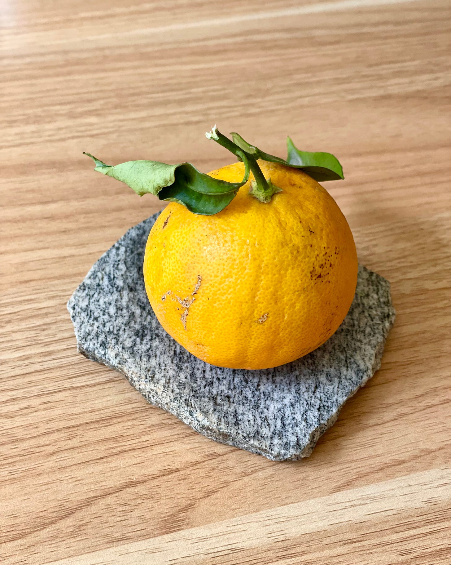 Whole orange sitting on a granite coaster on a table top