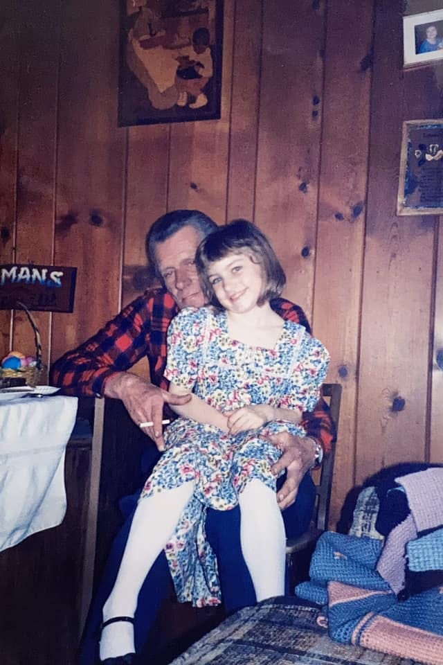 A photo of the author at about age five sitting on her grandfather's lap in a wood paneled room.