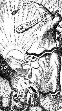 Black-and-white cartoon of a KKK member swinging a club with the words "The Ballot." Beneath The Klan member is the hand of an ape depicting the Roman Catholic Church.