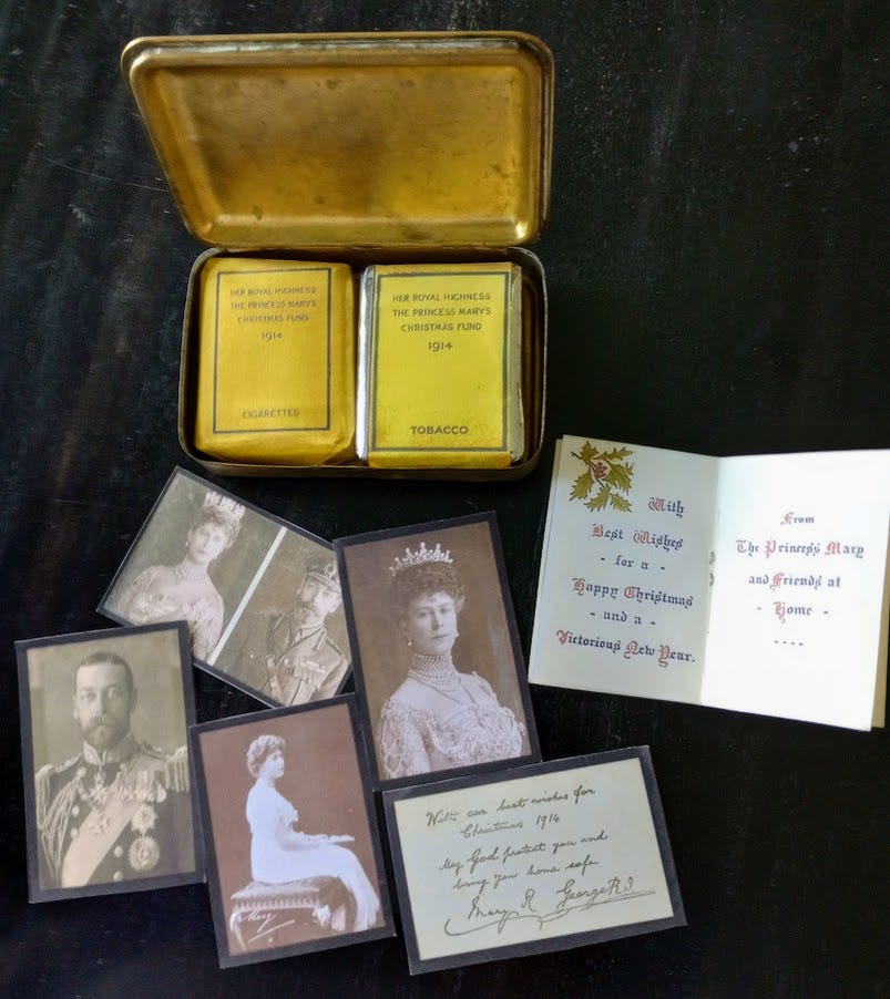 Open tin containing pack of pipe tobacco and a pack of cigarettes, along with paper contents 